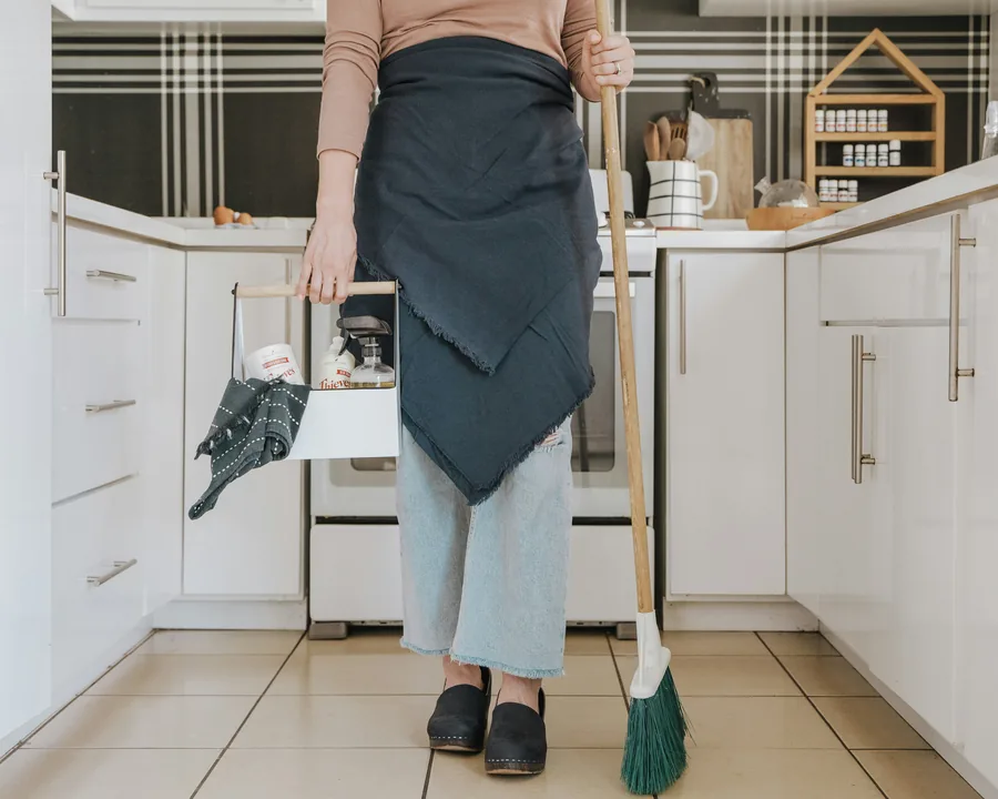 A cleaner's apron, caddy and broom in a home kitchen