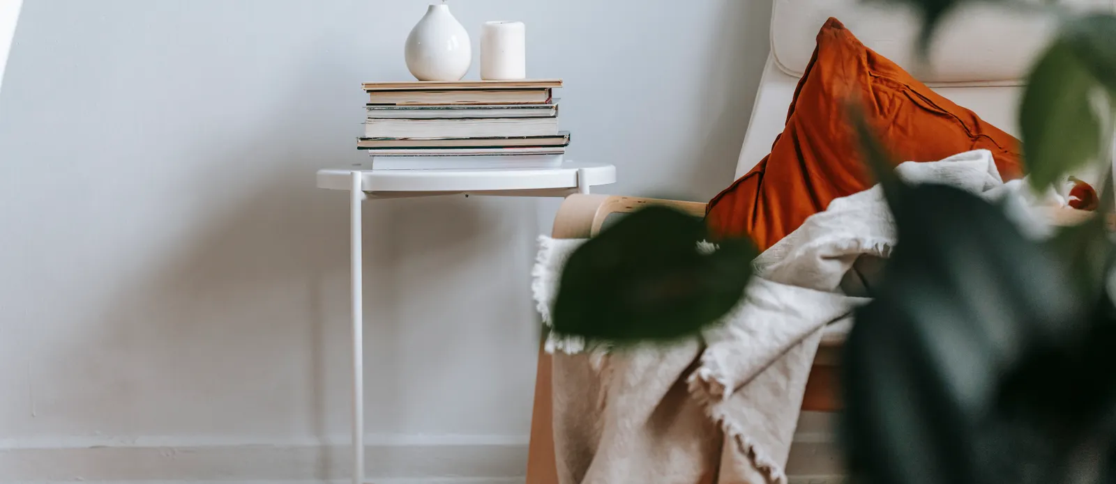 A quiet corner of a living room, with a folded throw, books and a vase